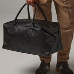 Load image into Gallery viewer, A person is holding a black leather duffel bag with a zipper closure.