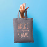 Load image into Gallery viewer, Grey Bride Squad mini tote bag with rose gold text held up against a blue background