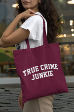 Load image into Gallery viewer, Woman carrying a burgundy True Crime Junkie cotton tote bag over her shoulder