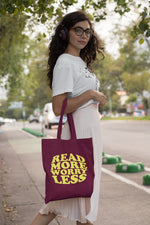 Load image into Gallery viewer, Woman carrying a burgundy Read More Worry Less cotton tote bag over her shoulder