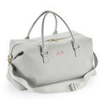 Load image into Gallery viewer, A gray leather duffel bag with a gold zipper and handles, featuring a personalized monogram on the front.
