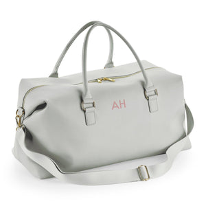 A gray leather duffel bag with a gold zipper and handles, featuring a personalized monogram on the front.
