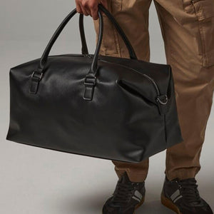 A person is holding a black leather duffel bag with a zipper closure.