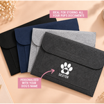 Load image into Gallery viewer, Four felt document pouches in black, navy, light gray, and dark gray are arranged on a peach background. The front dark gray pouch is personalized with a white paw print and the name 'DEXTER'.
