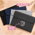 Load image into Gallery viewer, Four personalized felt pet document pouches in black, navy blue, and heather gray, arranged diagonally on a beige background with decorative pearl flowers. Pink text overlays highlight the product's use for storing dog documents and its personalization option.
