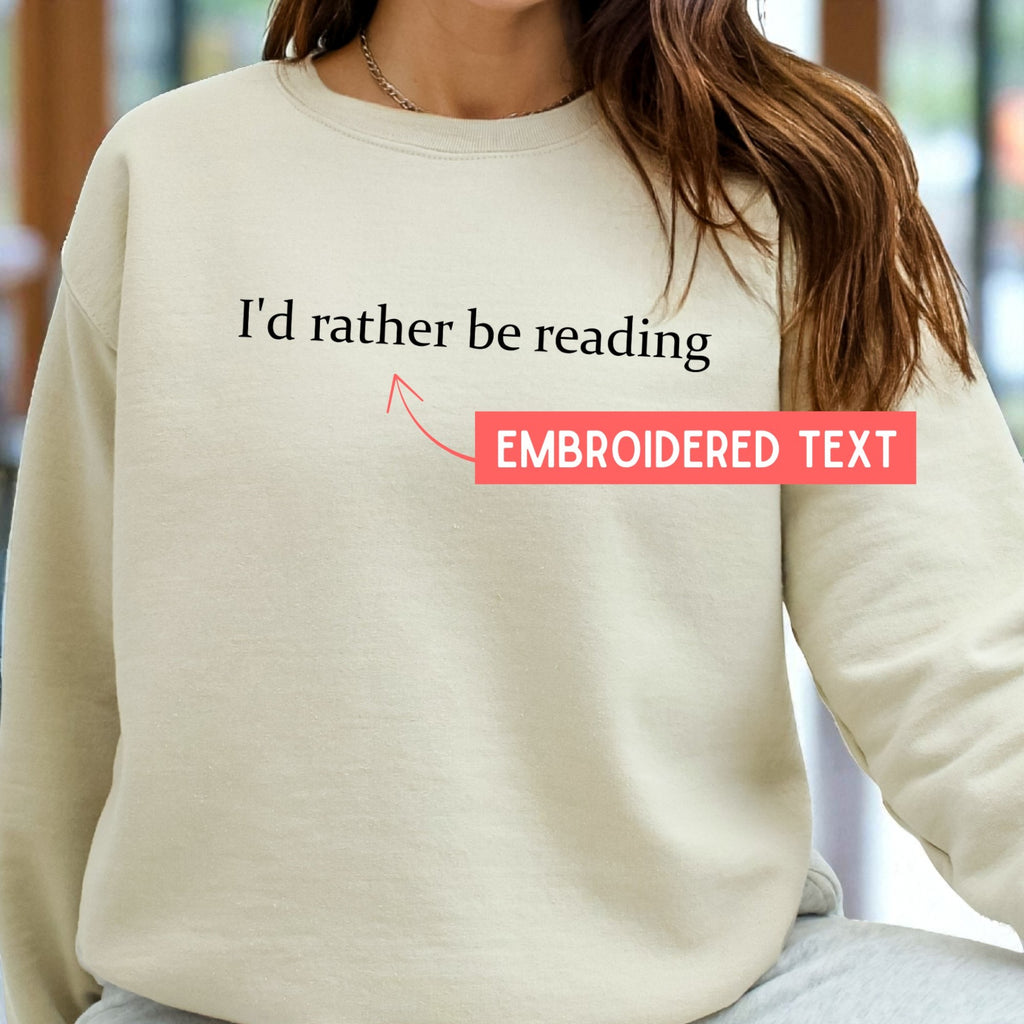 Beige sweatshirt with 'I'd rather be reading' text and an arrow pointing to it, with a blurred background.