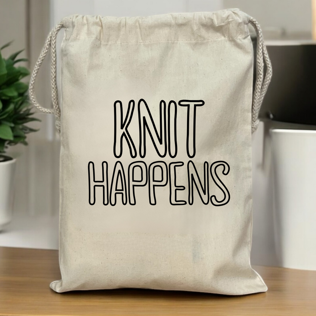 Beige drawstring bag with 'KNIT HAPPENS' text on a wooden surface.