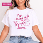 Load image into Gallery viewer, A woman wearing a white short-sleeve graphic T-shirt with pink text reading 'I'm The Tying Knift' and smaller text 'ABIGAIL'S HEN FUENGIROLA 2027', paired with light blue jeans. A pink label in the top left says 'PINK TEXT'.
