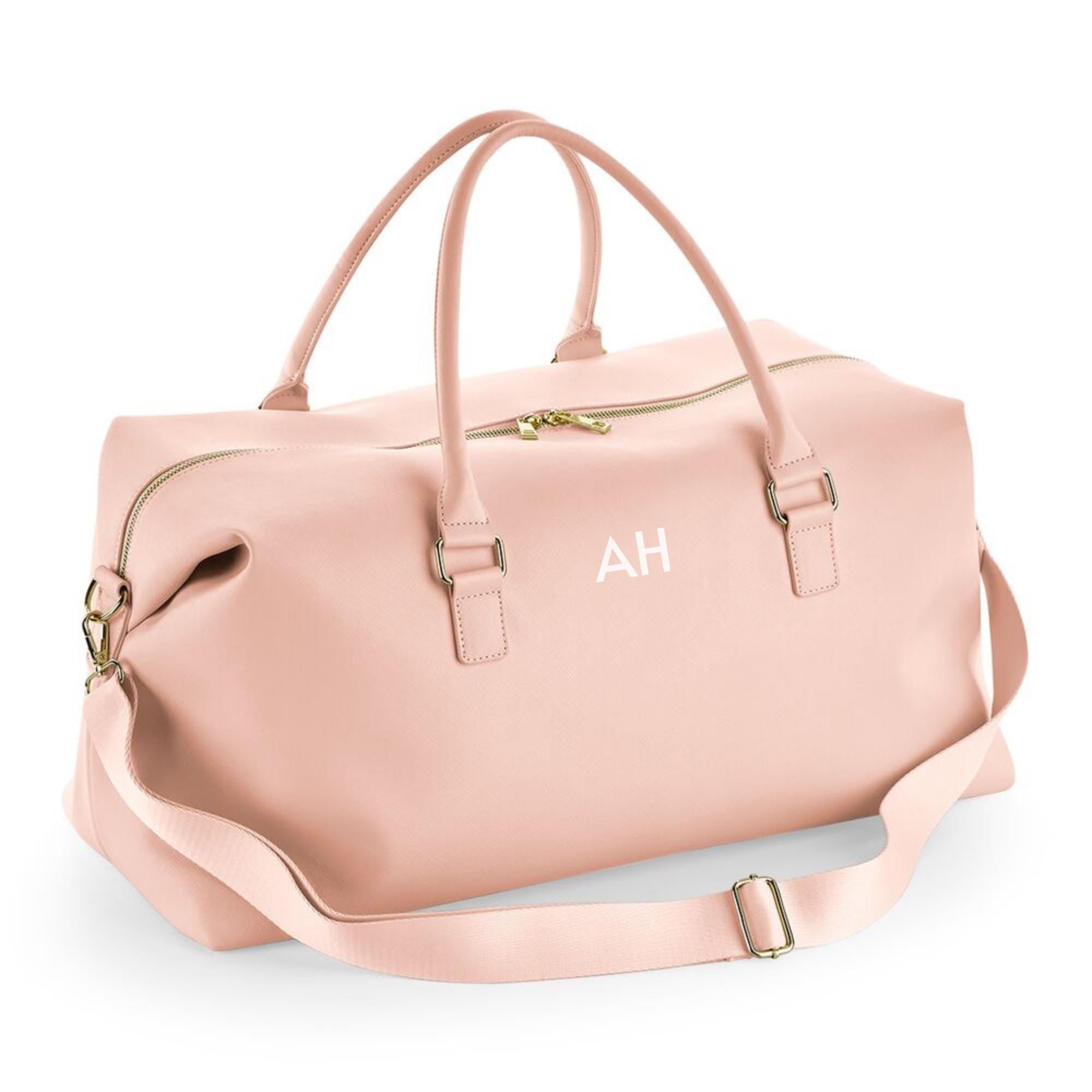 A pink leather duffel bag with a gold zipper and handles, featuring a personalized monogrammed logo on the front.