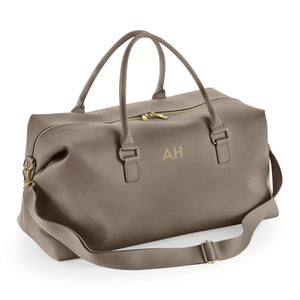 A tan leather duffel bag with a gold zipper and handles, featuring a personalized monogrammed logo on the front.