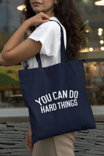Load image into Gallery viewer, Woman carrying a navy You Can Do Hard Things cotton tote bag over her shoulder
