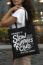 Load image into Gallery viewer, Woman carrying a black Slow Runners Club cotton tote bag over her shoulder
